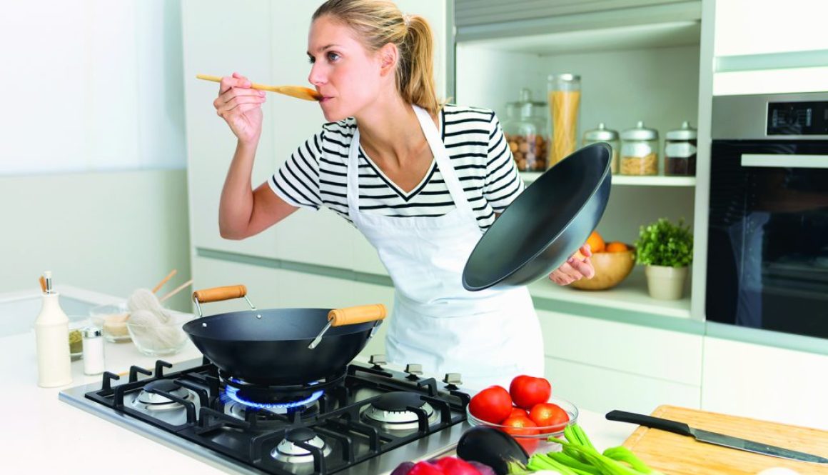 Healthy young woman cooking and tasting food with wooden spoon i