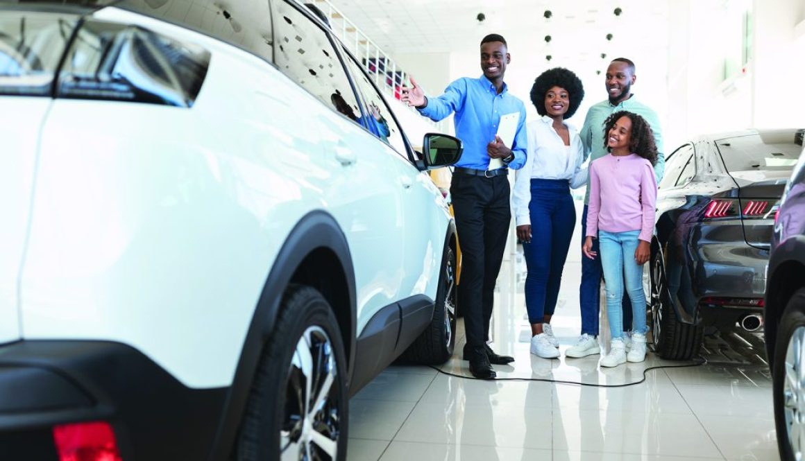 Automobile seller showing luxury car to young black family at auto dealership