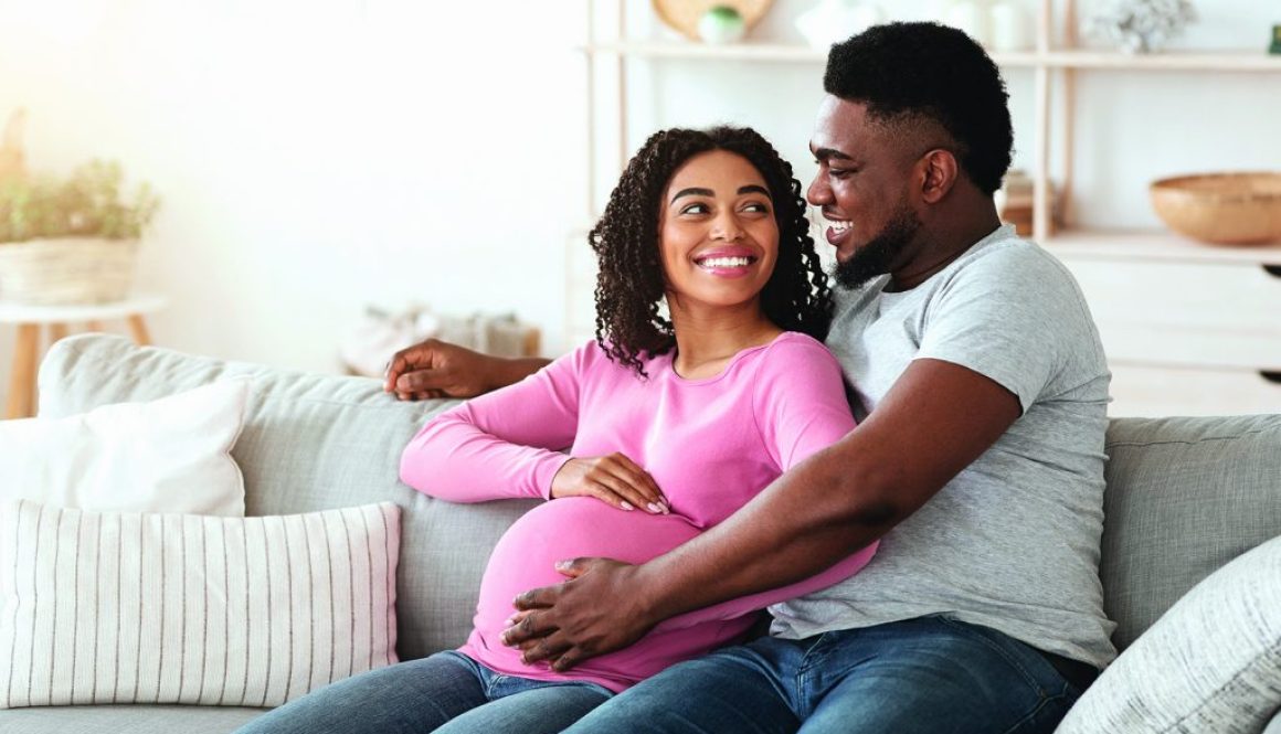 Lovely happy expecting african parents sitting on sofa at home