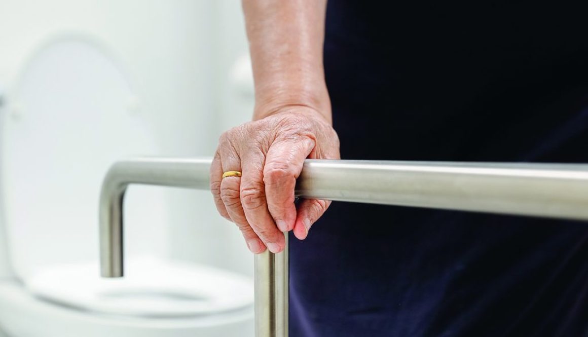 Elderly woman holding on handrail in bathroom.