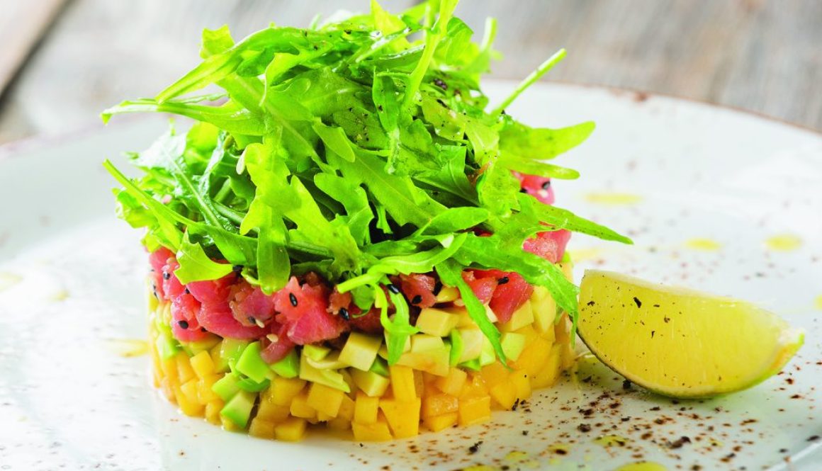 Delicious avocado, mango and raw salmon salad, tartare, served on a white plate with lime