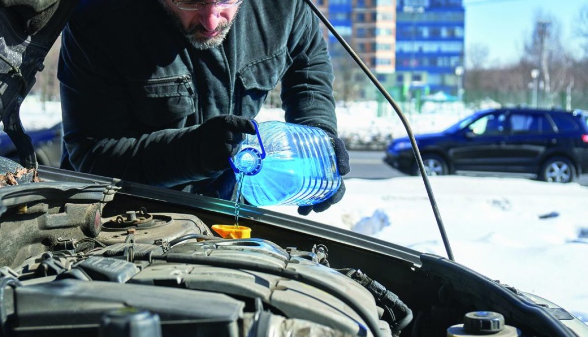 Man filling a windshield washer tank of a car by antifreeze on winter Moscow street