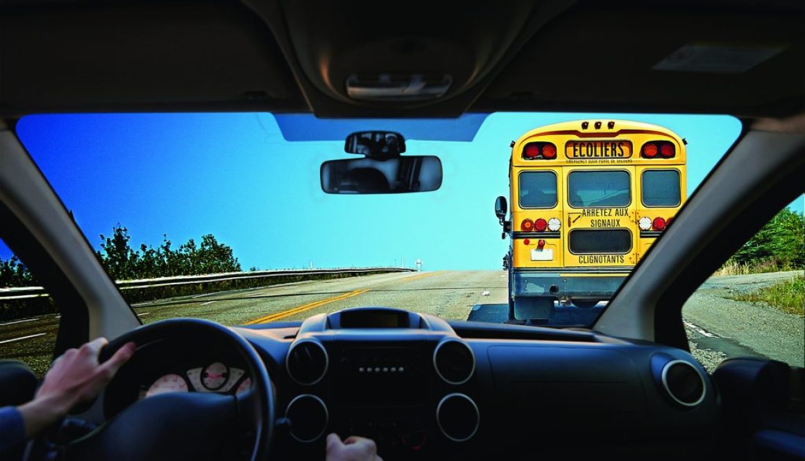 Young driver inside a car following a Yellow bus school