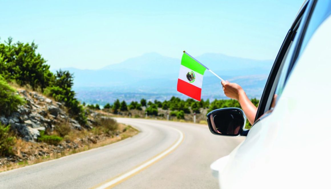 Woman holding Mexico flag from the open car window driving along the serpentine road in the mountains. Concept