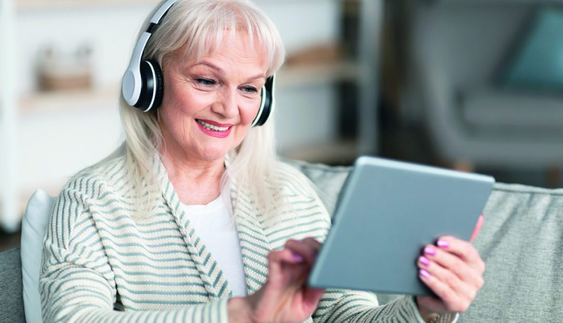 Smiling mature woman in headset using tablet sitting on sofa