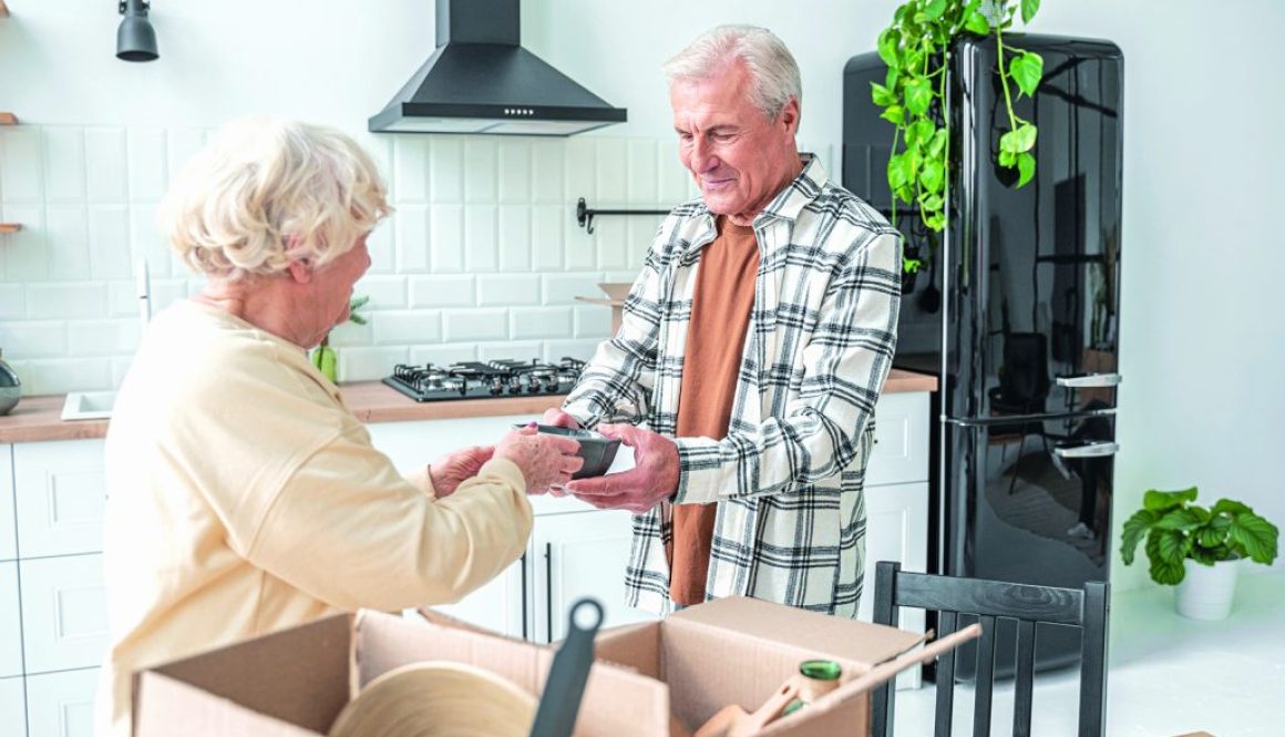 Elderly woman taking plate from her senior husband while unpacking boxes